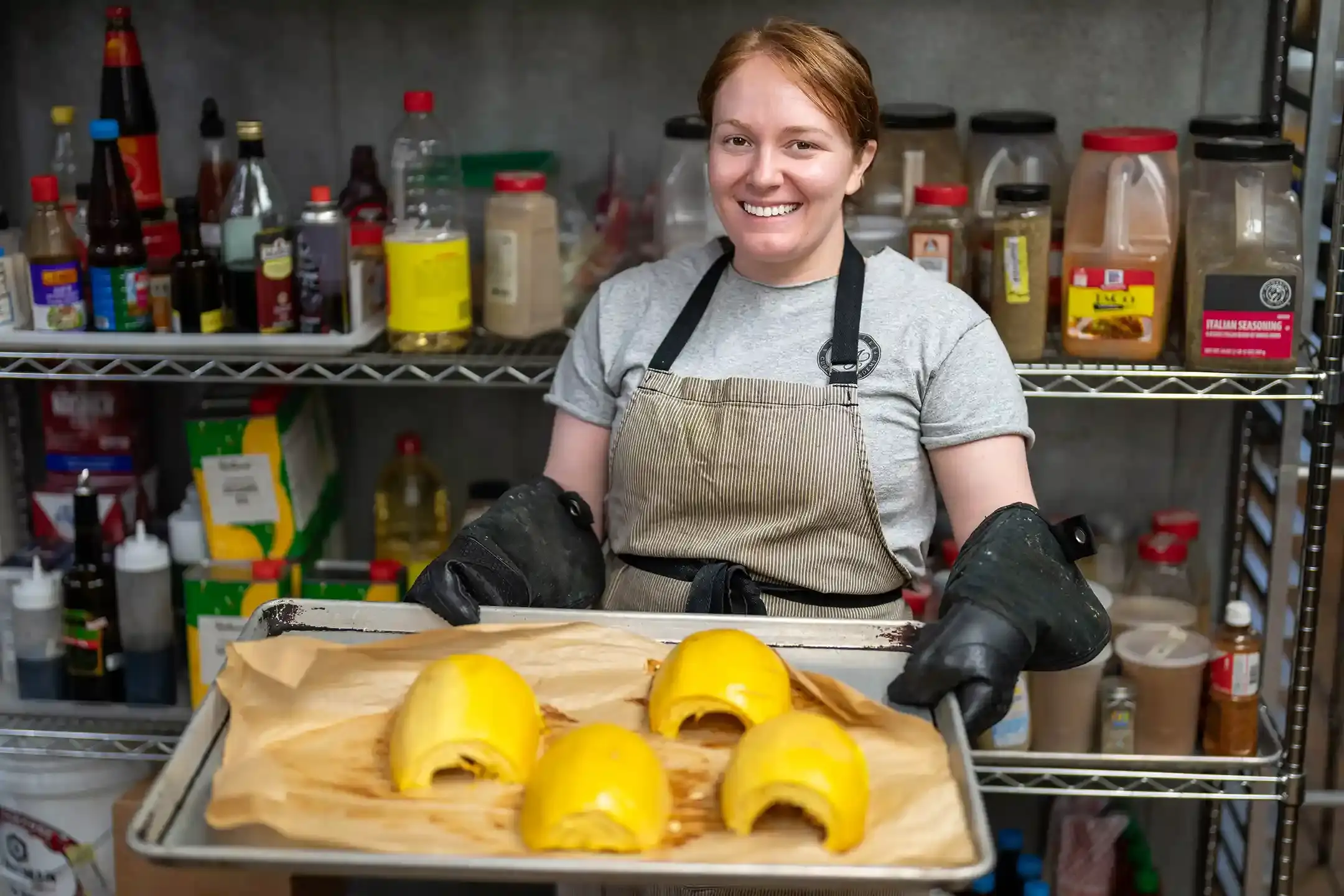 An image of a woman chef smiling with a tray of cooked squash